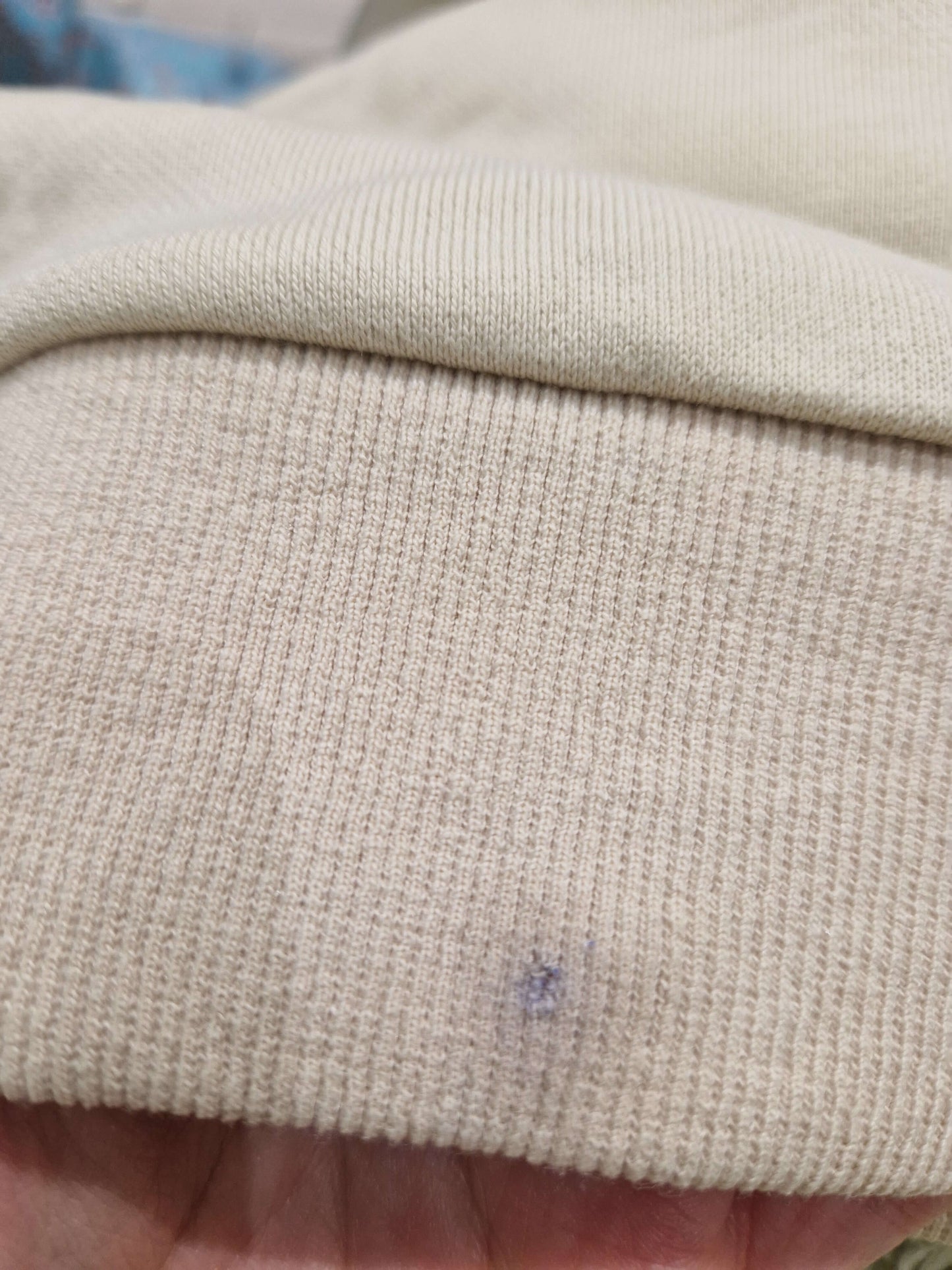 A close up of the back of the beige Surviving jumper with a small pen mark and hole in the bottom rim
