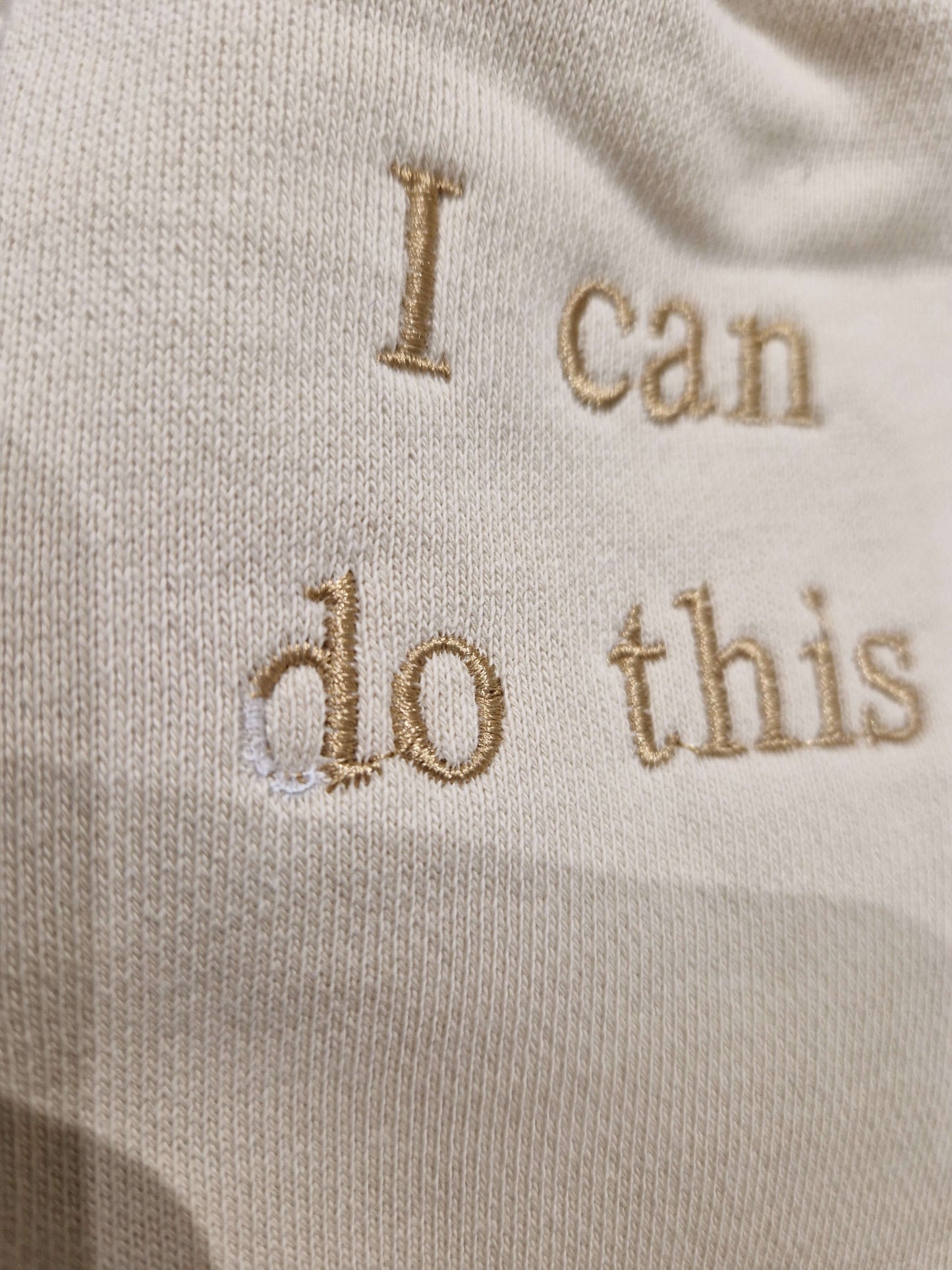 A close up of the cuff of the sleeve that reads 'I can do this ' it has a small defect in the 'd' where the embroidery has made a full 'd'
