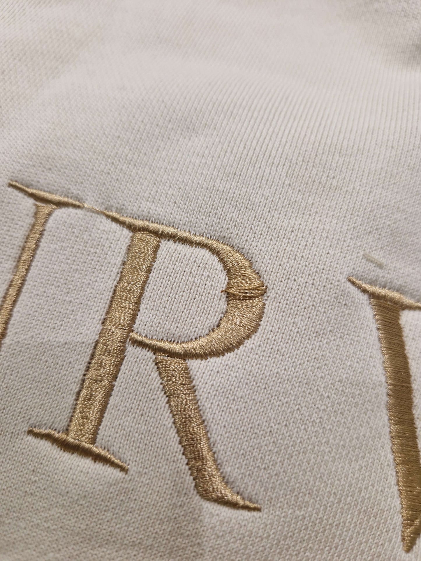 A close up of the beige Surviving jumper with a embroidery pull in the 'R' letter