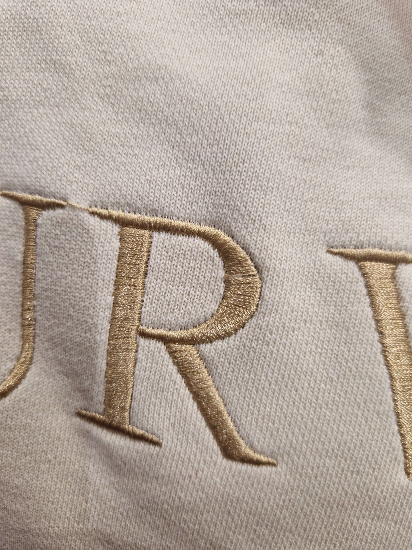 A close up of the beige Surviving jumper with a embroidery pull in the 'R' letter