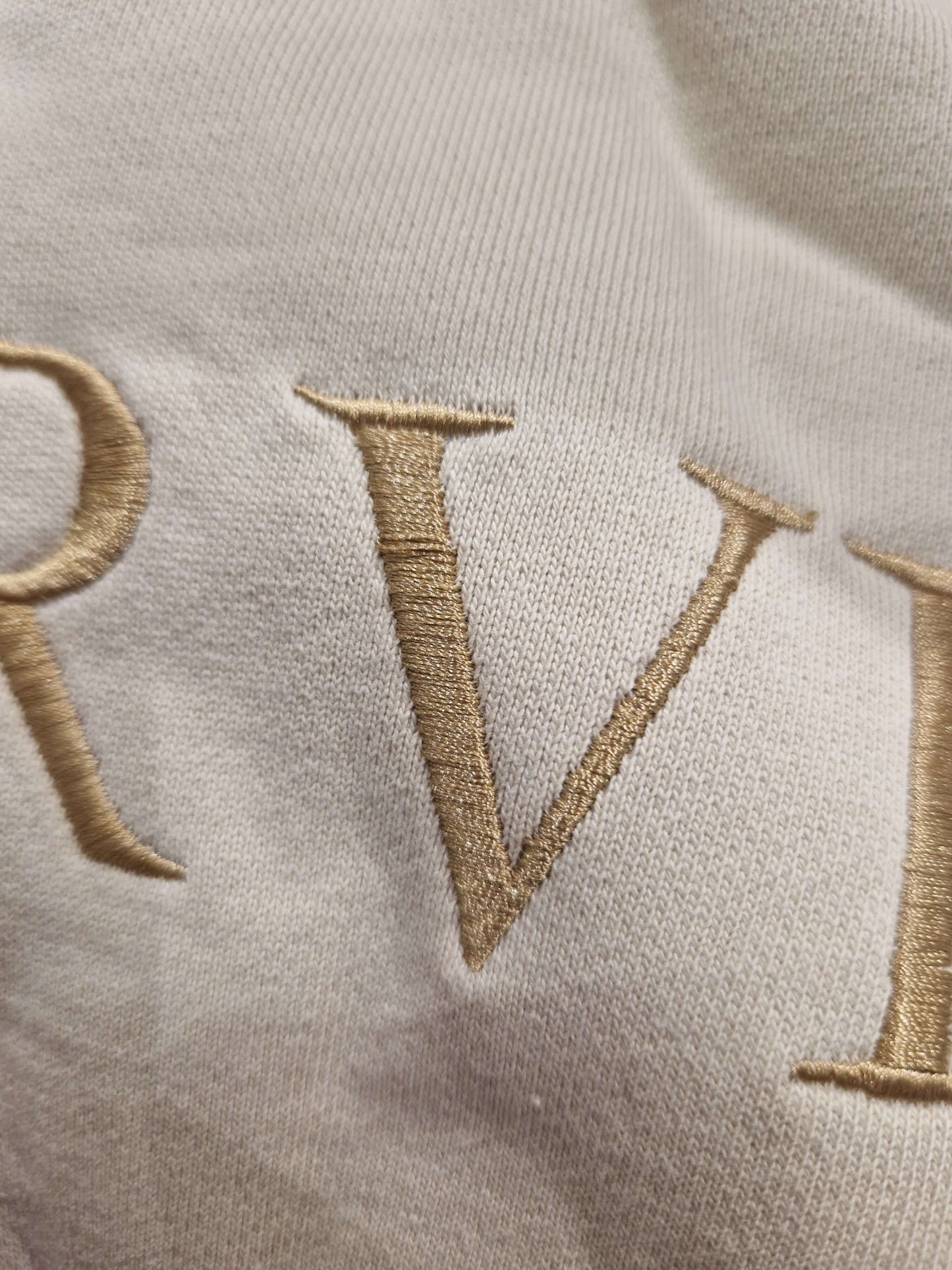 A close up of the beige Surviving jumper with a embroidery pull in the 'V' letter