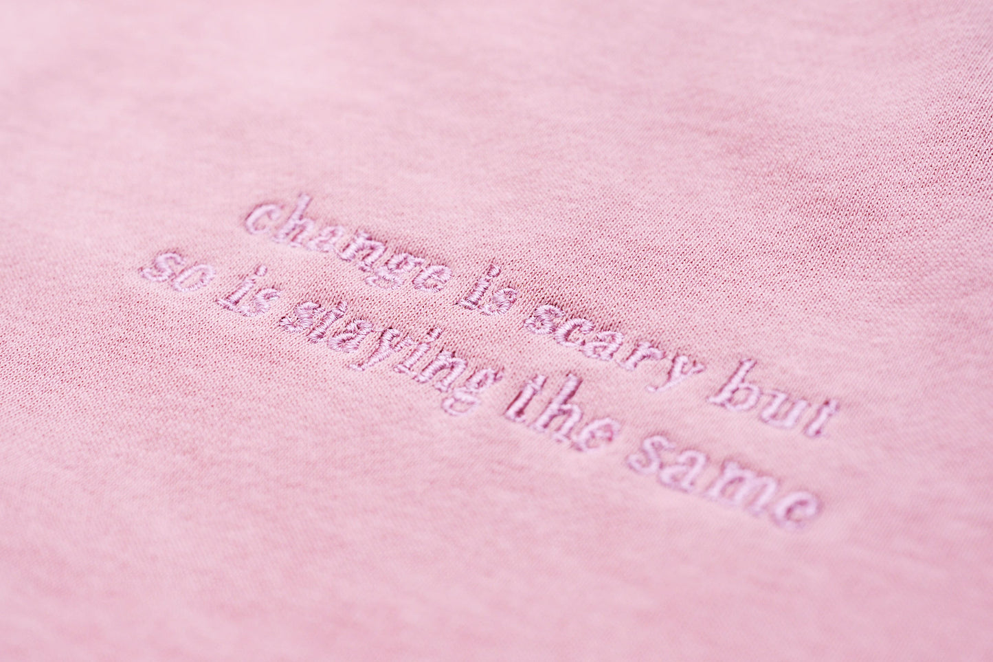 Close-up of a dusty pink embroidered jumper with the logo "Change is scary but so is staying the same" across the chest, part of our mental health clothing collection.
