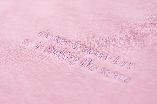 Close-up of a dusty pink embroidered jumper with the logo "Change is scary but so is staying the same" across the chest, part of our mental health clothing collection.