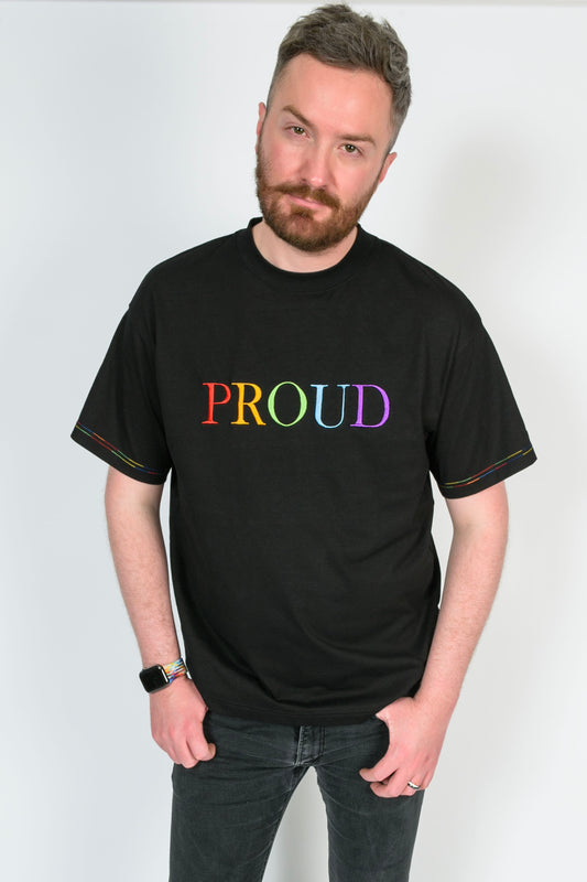 A beautiful black high quality oversized t-shirt with a bright rainbow letters spelling out 'Proud'. The stitching on the t-shirt sleeves has bright rainbow stitching.
