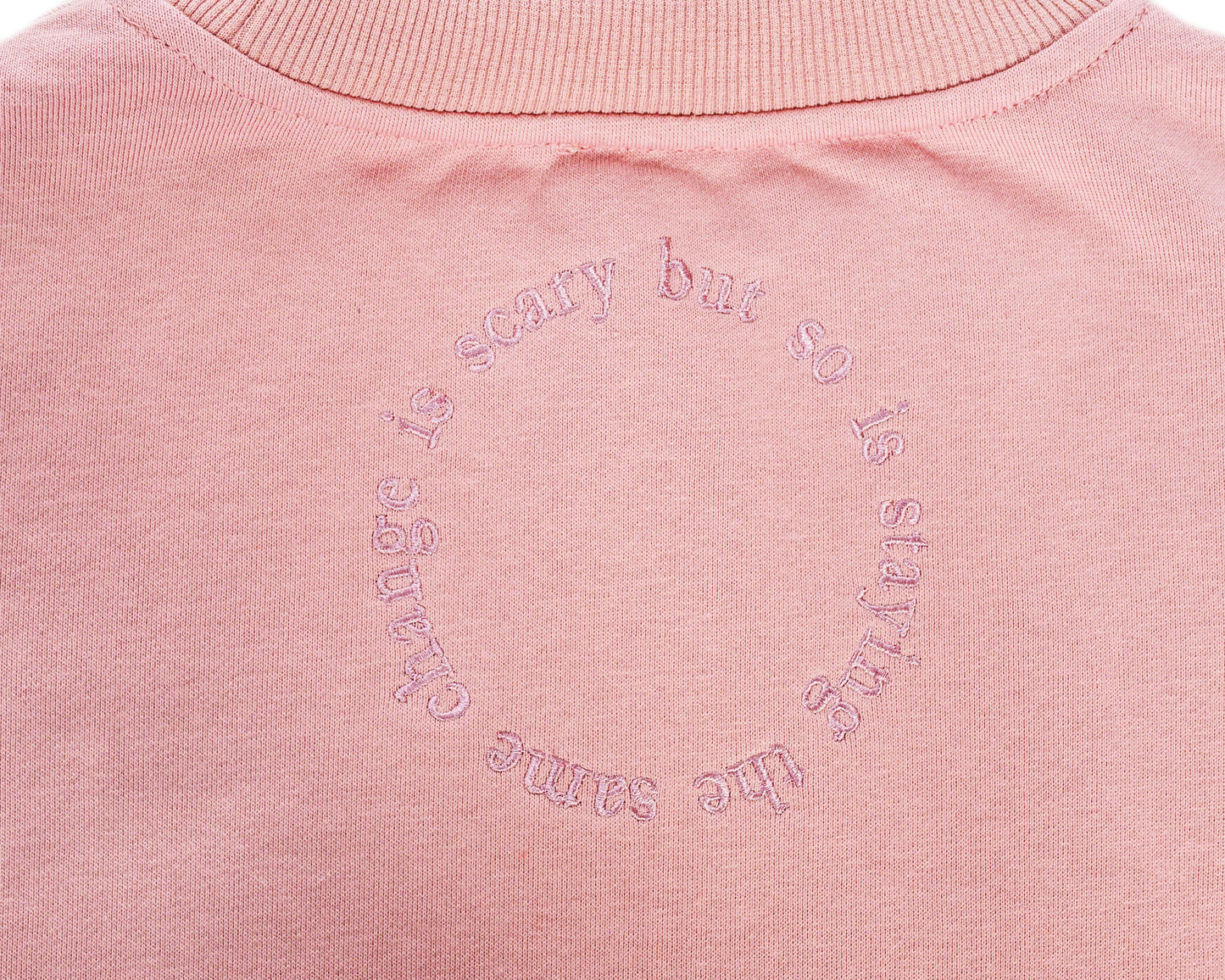 Close-up of the back of a dusty pink embroidered jumper featuring a large embroidered circle with the message "Change is scary but so is staying the same," a key piece in our mental health clothing collection.