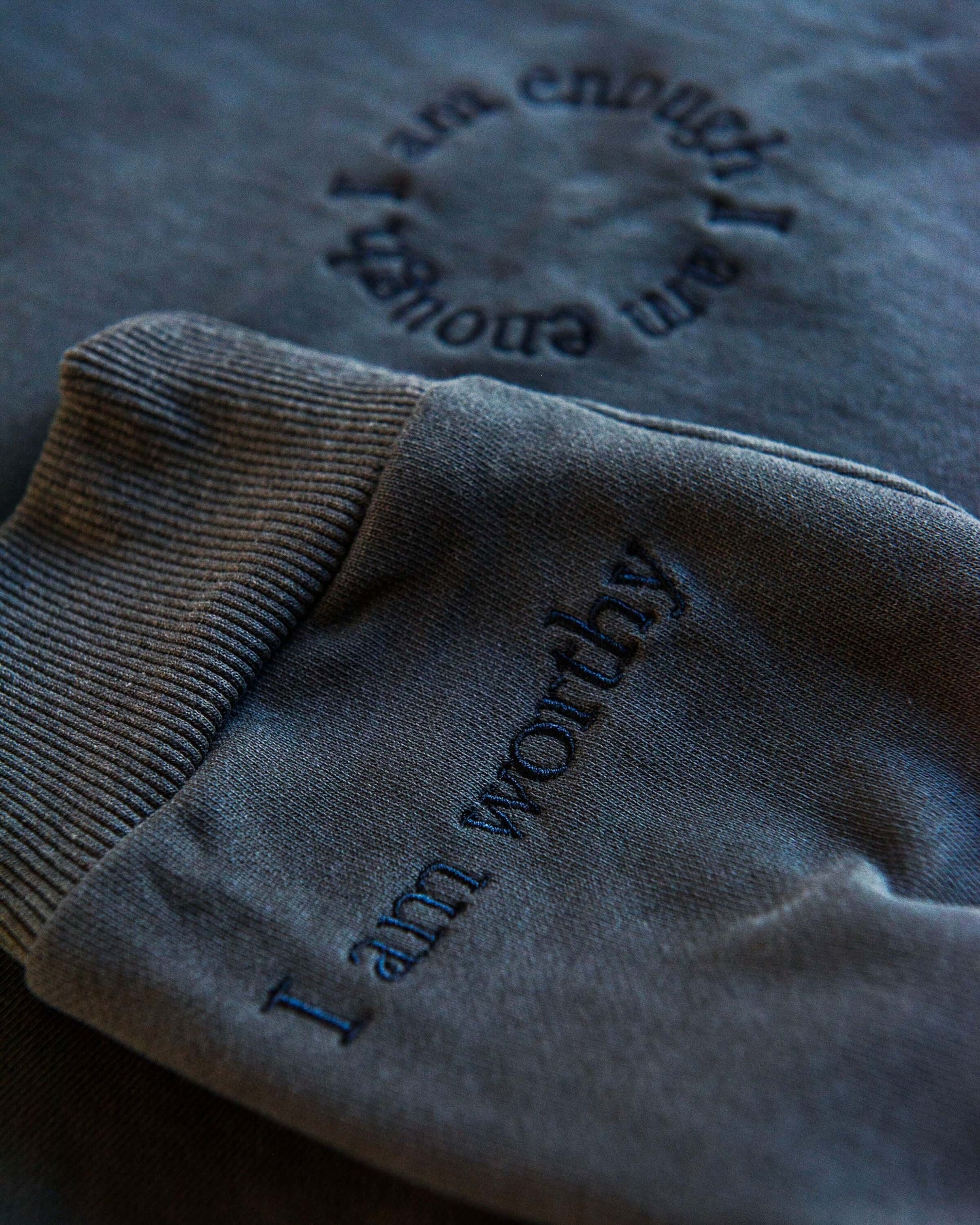 A slate grey, cotton oversized jumper with beautiful slate embroidery it reads'I am Enough' in a circle over the chest and has reassuring messages on the cuffs that read 'I am Loved' and 'I am Worthy'