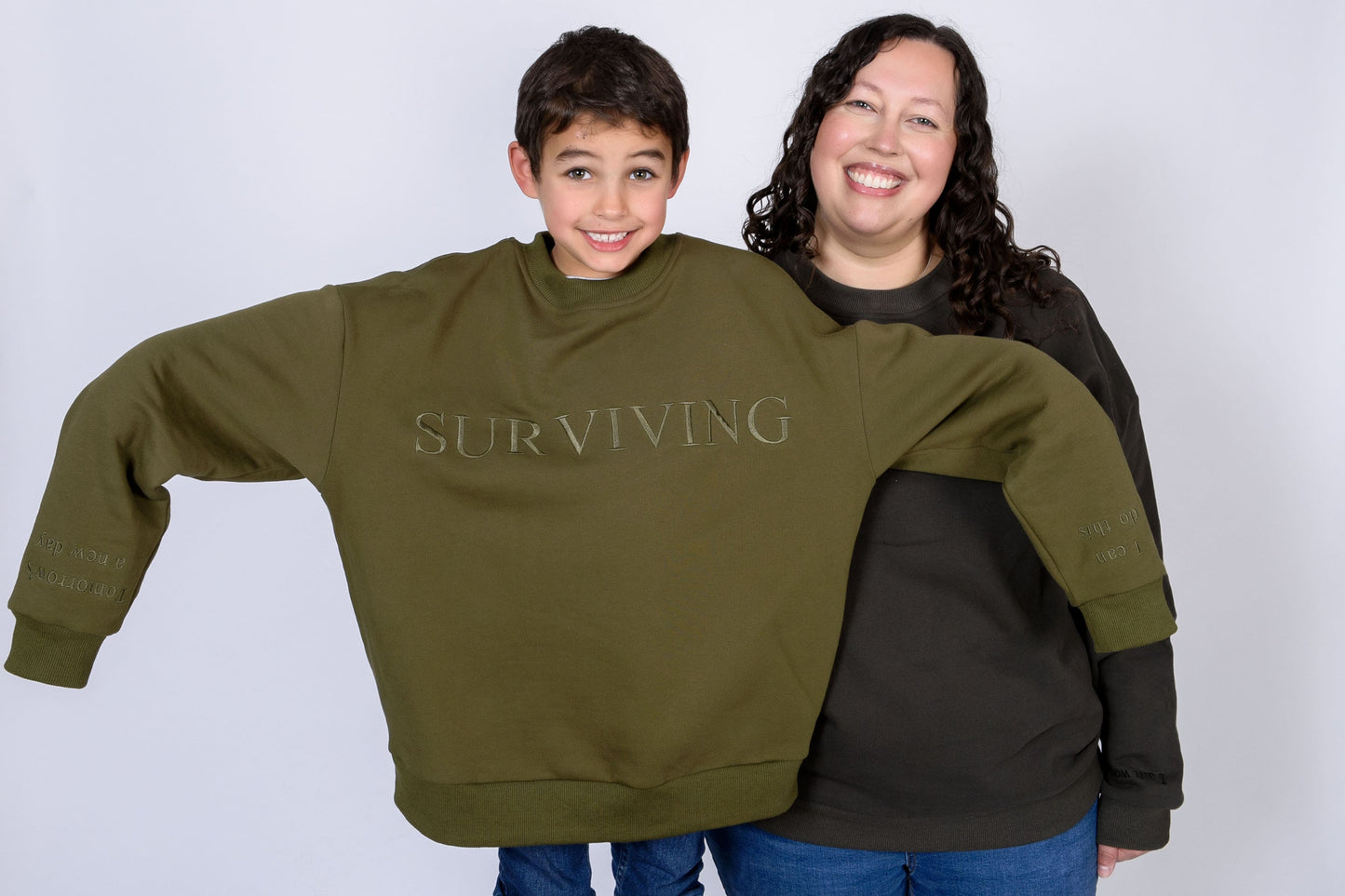 Our Surviving khaki green embroidered jumper from our mental health clothing collection, featuring the uplifting message "Surviving" across the chest. Additional encouraging phrases include "Tomorrow's a new day" and "I can do this," elegantly stitched to inspire resilience.