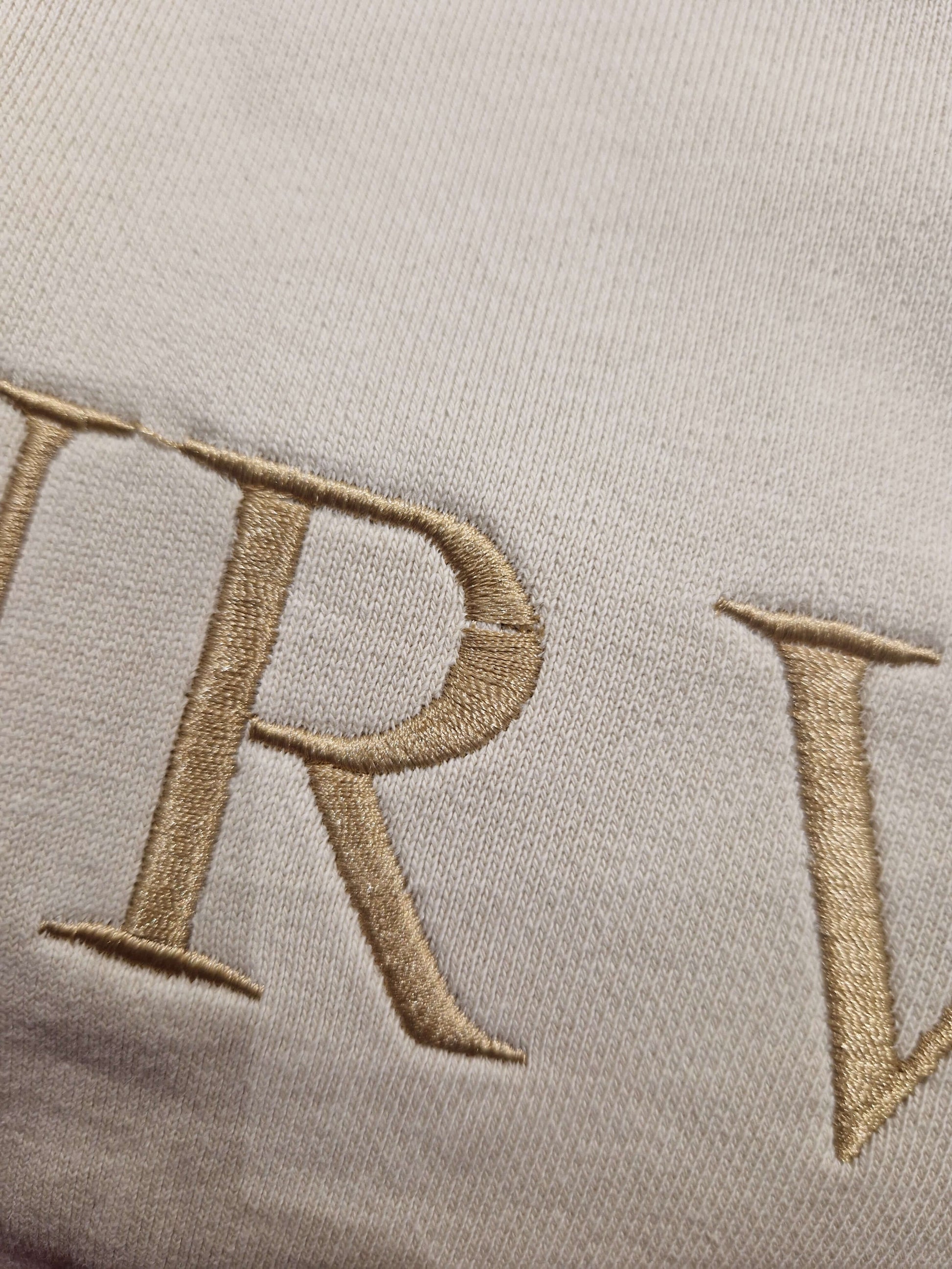 A close up of the beige Surviving jumper with a embroidery pull in the 'R' letter