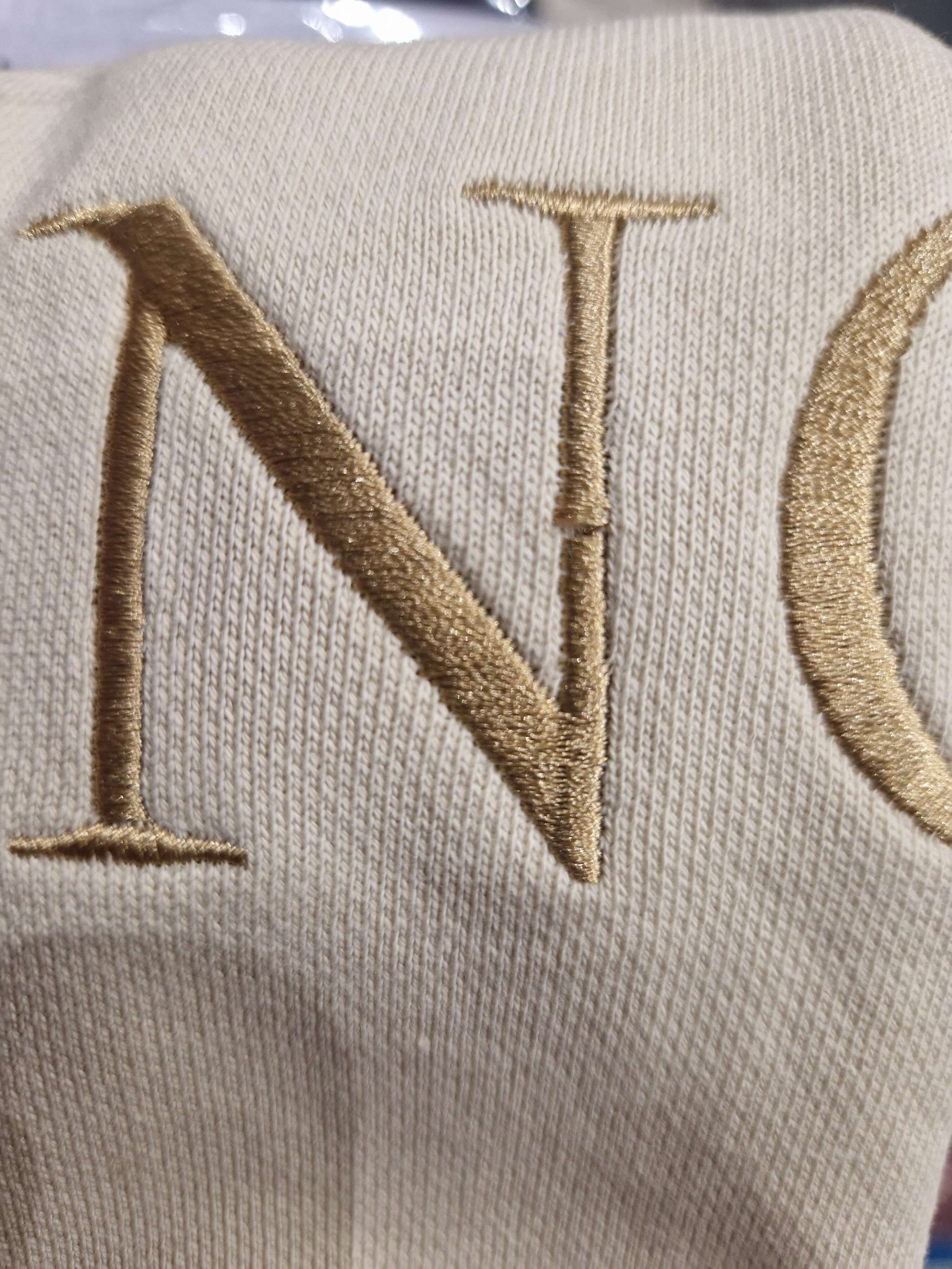 A close up of the beige Surviving jumper with a embroidery pull in the 'N' letter