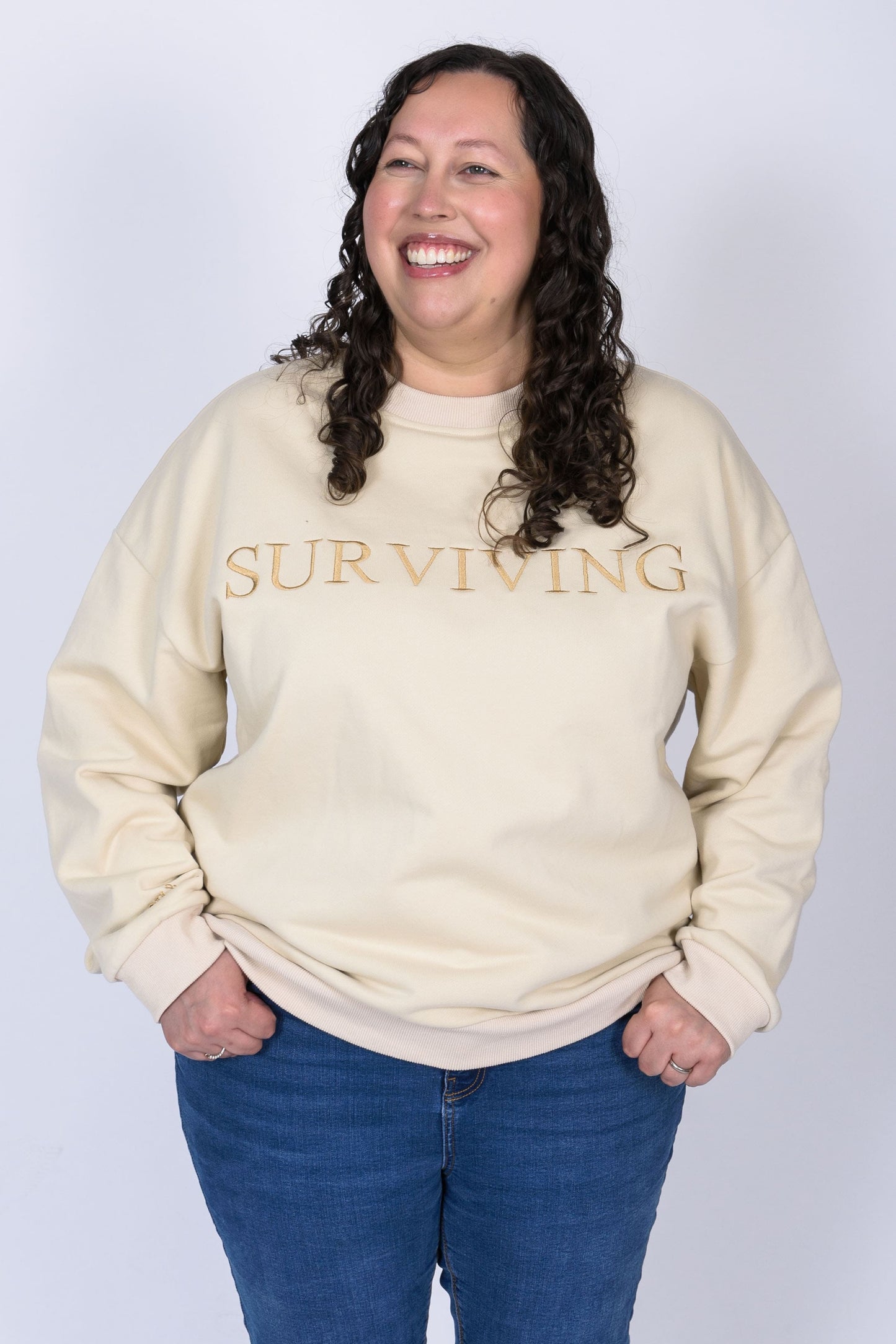 Our Surviving beige embroidered jumper from our mental health clothing collection, featuring the uplifting message "Surviving" across the chest and phrases include "Tomorrow's a new day" elegantly stitched to inspire resilience.