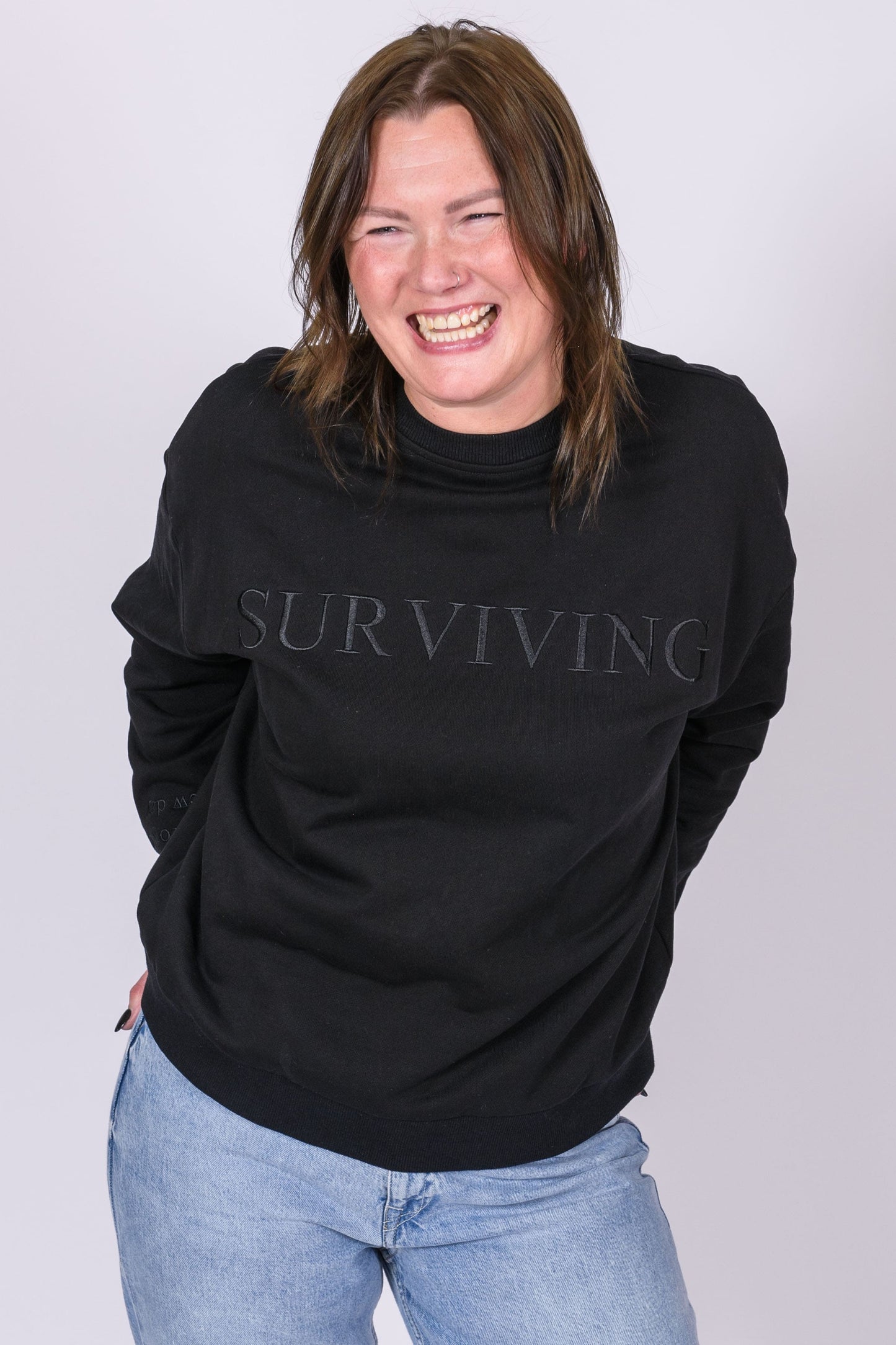 Our Surviving black embroidered jumper from our mental health clothing collection, featuring the uplifting message "Surviving" across the chest. Additional encouraging phrases include "Tomorrow's a new day" and "I can do this," elegantly stitched to inspire resilience.