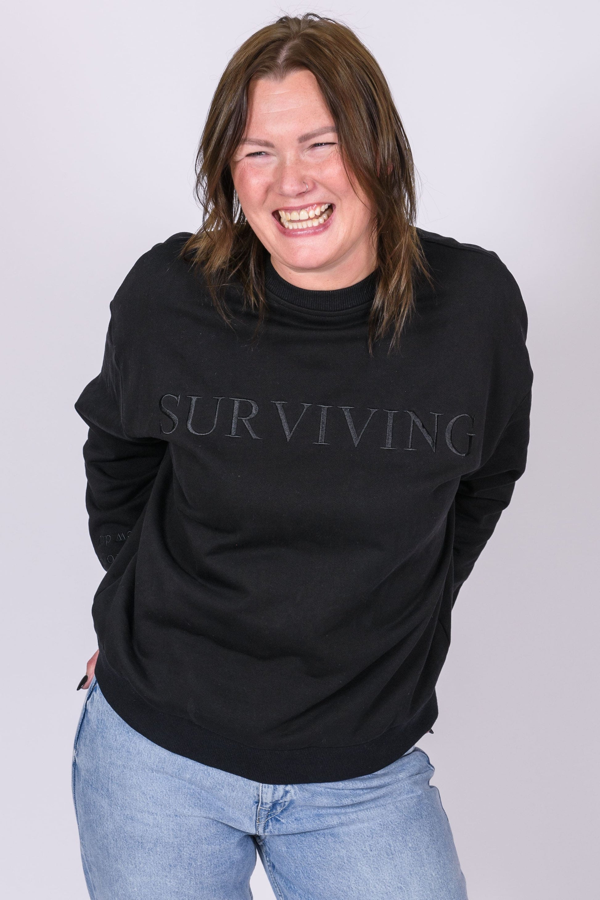 Our Surviving black embroidered jumper from our mental health clothing collection, featuring the uplifting message "Surviving" across the chest. Additional encouraging phrases include "Tomorrow's a new day" and "I can do this," elegantly stitched to inspire resilience.