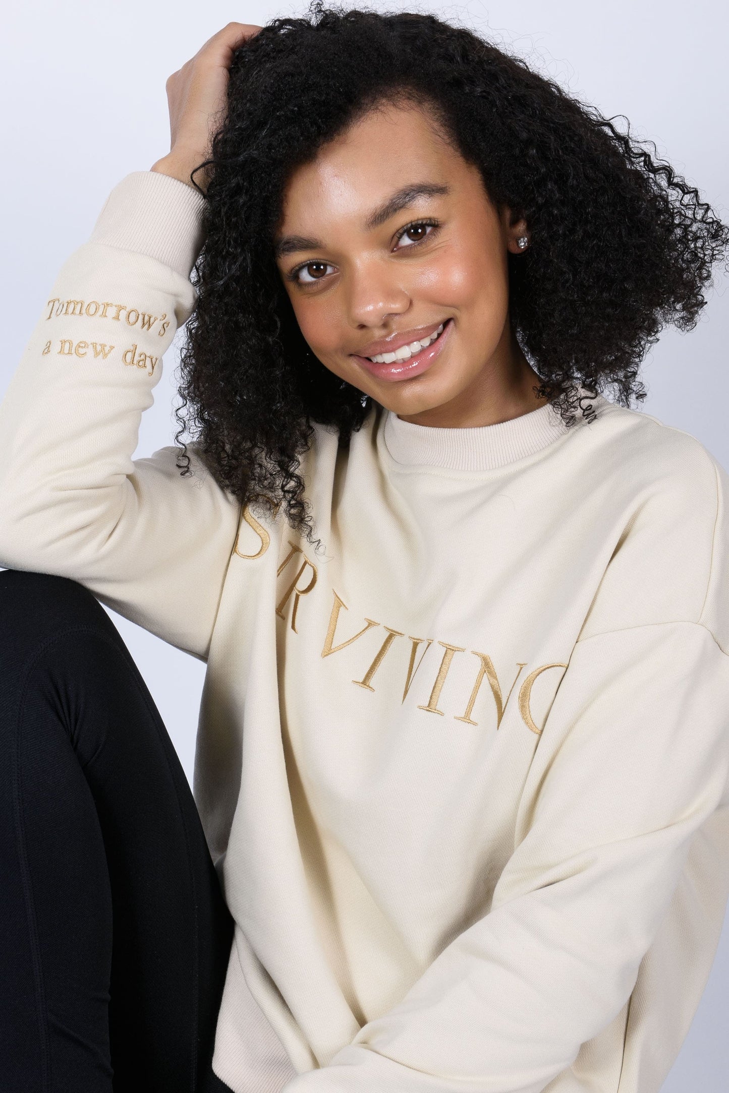 Our Surviving beige embroidered jumper from our mental health clothing collection, featuring the uplifting message "Surviving" across the chest and phrases include "Tomorrow's a new day" elegantly stitched to inspire resilience.